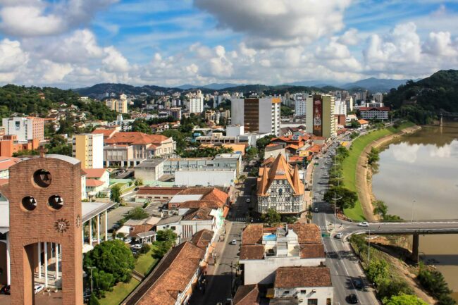 Vista panorâmica do centro de Blumenau, com a Torre da Matriz em primeiro plano e a prefeitura e ponte de ferro ao fundo