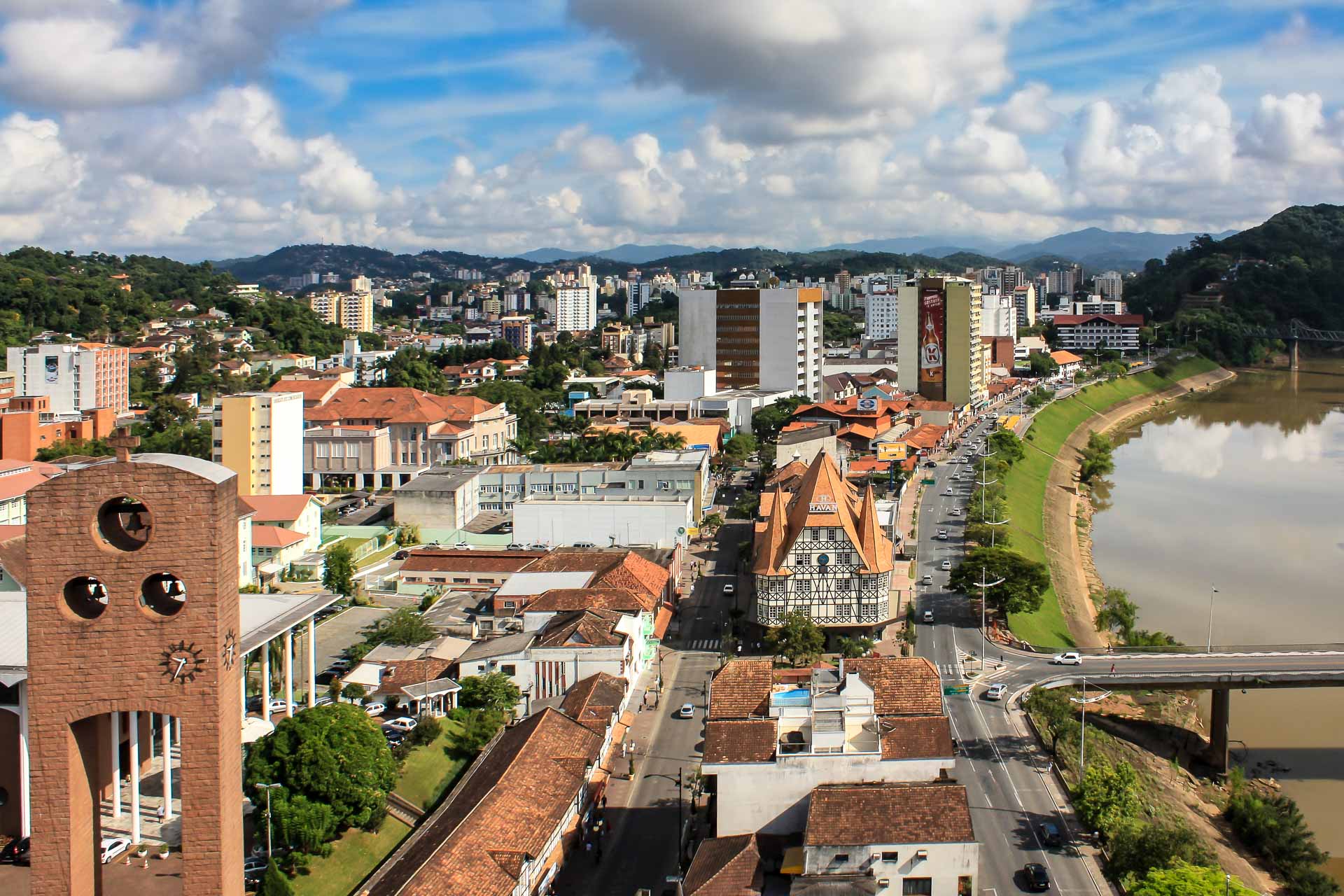 Vista panorâmica do centro de Blumenau, com a Torre da Matriz em primeiro plano e a prefeitura e ponte de ferro ao fundo